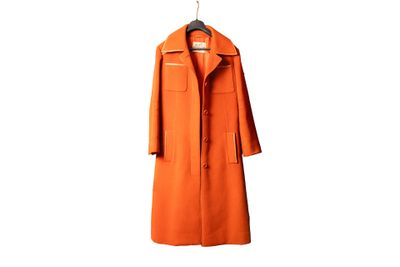 un manteau orange suspendu à un cintre sur un mur blanc