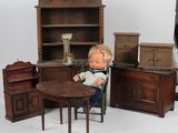 une poupée assise à une table devant un ensemble de meubles