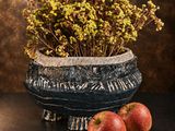 two apples sitting next to a vase of flowers on a table