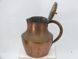 a copper pitcher with a spoon in it on a white surface