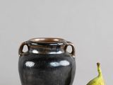 un petit vase noir posé à côté d'une poire sur une table