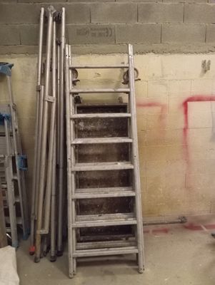 une échelle appuyée contre un mur, à côté d'un tas de tuyaux métalliques