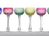 six verres à vin colorés alignés en rang sur une surface blanche