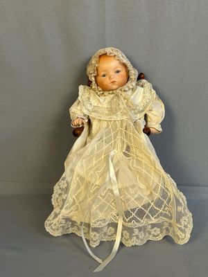 une poupée à l'ancienne assise sur une chaise en bois, vêtue d'une robe blanche et d'un bonnet