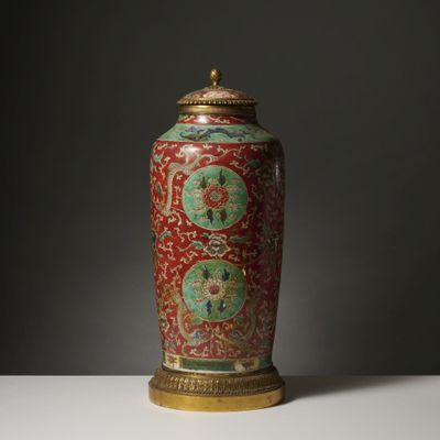 une image représentant un vase rouge muni d'un couvercle doré, posé sur une table
