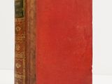 an old book with a red cover sitting on a white surface