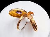 a gold ring with a purple stone in it on a white plate