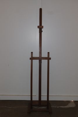 a wooden easel in the corner of a room with a white wall