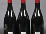 three bottles of red wine are lined up on a gray surface
