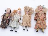 four antique dolls are lined up in a row on a white surface