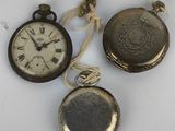 three antique pocket watches are displayed on a white surface