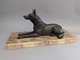 statue d'un chien couché sur un socle en marbre, sur fond gris