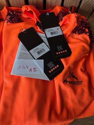 an orange shirt with two tags on it sitting on top of a chair
