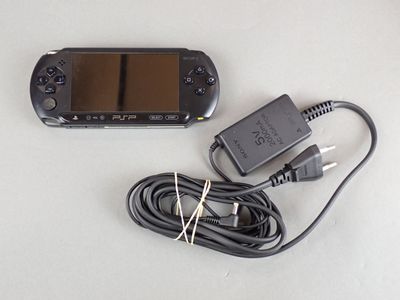 a black game console and a charger on a white table