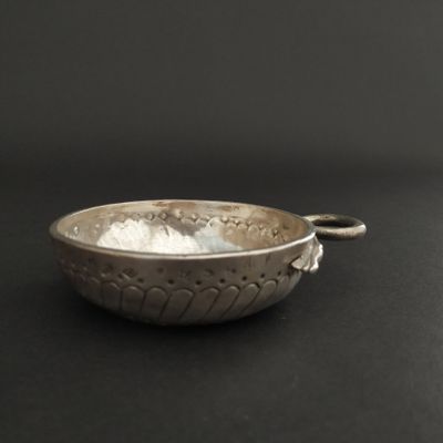 a silver bowl with a handle on a black surface
