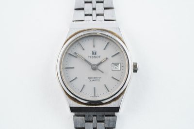 une montre en argent avec un cadran blanc sur une surface blanche