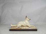 a white dog figurine sitting on top of a wooden base