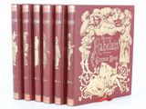 quatre livres rouges ornés d'illustrations dorées, posés sur une surface blanche
