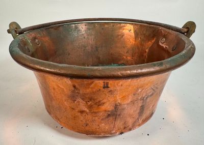 une grande casserole en cuivre avec des poignées, posée sur une surface blanche