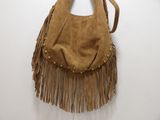 tan sued purse with fringes and studded handles hanging on a wall