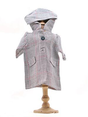 une poupée vêtue d'un manteau et d'un chapeau, posée sur un socle en bois