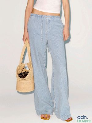 a woman in a white top and blue pants holding a straw bag