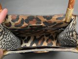 someone is holding a leopard print purse with a wooden handle