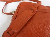 an orange leather purse with a strap on a white surface