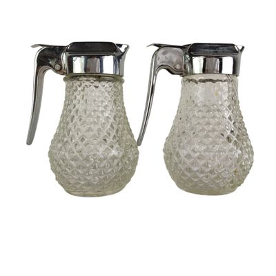 two clear glass pitchers with metal handles on a white background