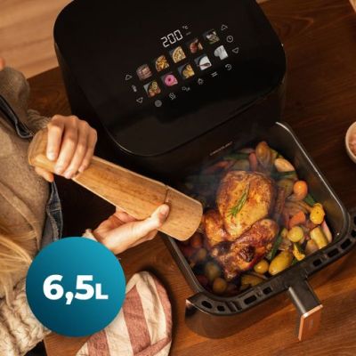 une femme en train de préparer un repas dans une friteuse à air chaud posée sur une table en bois