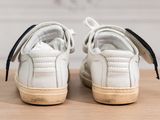 white leather sneakers with black laces on a wooden surface