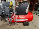a red air compressor sitting in a garage with a black bag on top of it