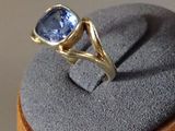 une bague ornée d'une pierre bleue, posée sur un socle en bois