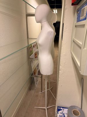 un mannequin blanc dans un coin d'une pièce, avec un rouleau de papier toilette par terre