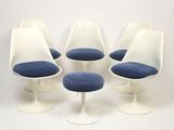 four white tulip chairs with blue cushions and a white stool