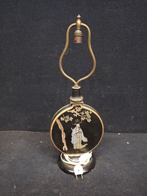 une image représentant une lampe de table noire et dorée sur laquelle est posée une femme
