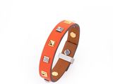 un bracelet en cuir orange orné de clous dorés sur fond blanc