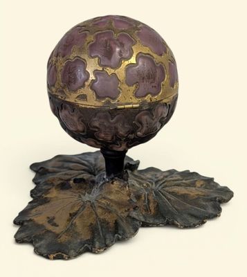 un œuf violet et doré posé sur un socle orné de feuilles