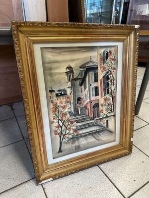 painting of a house in a gold frame sitting on a tile floor