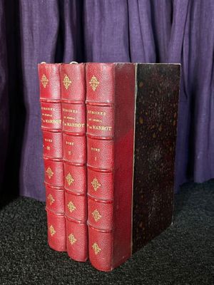 trois livres rouges posés sur une table noire, à côté d'un rideau violet