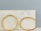 une paire de boucles d'oreilles créoles en or posée sur un bloc de marbre
