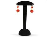a pair of red and gold earrings on a black stand