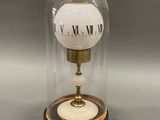 clock in a glass dome on a wooden base on a gray surface
