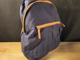 un sac à dos gris et orange posé sur une table en bois, avec un mur noir en arrière-plan