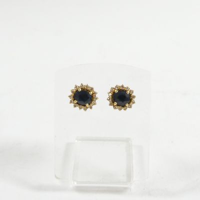 une paire de boucles d'oreilles noires et dorées présentées sur un présentoir transparent