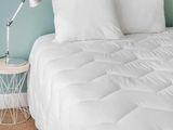 un lit recouvert d'une couette blanche et une table de chevet avec une lampe