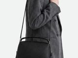 Une femme en tailleur gris tient un sac noir.