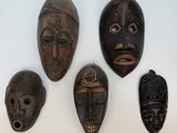 quatre masques en bois sont exposés sur une surface blanche
