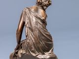 bronze statue of a woman sitting on a rock with her back to the camera