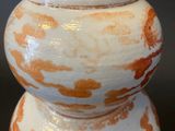 a white and orange vase sitting on a black surface